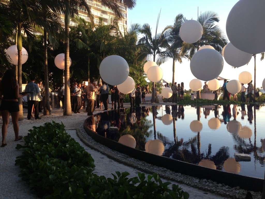 A fancy fine dining event at the Modern Honolulu hotel with balloons being reflected in the surface of the hotel pool and palm trees against a blue sky.