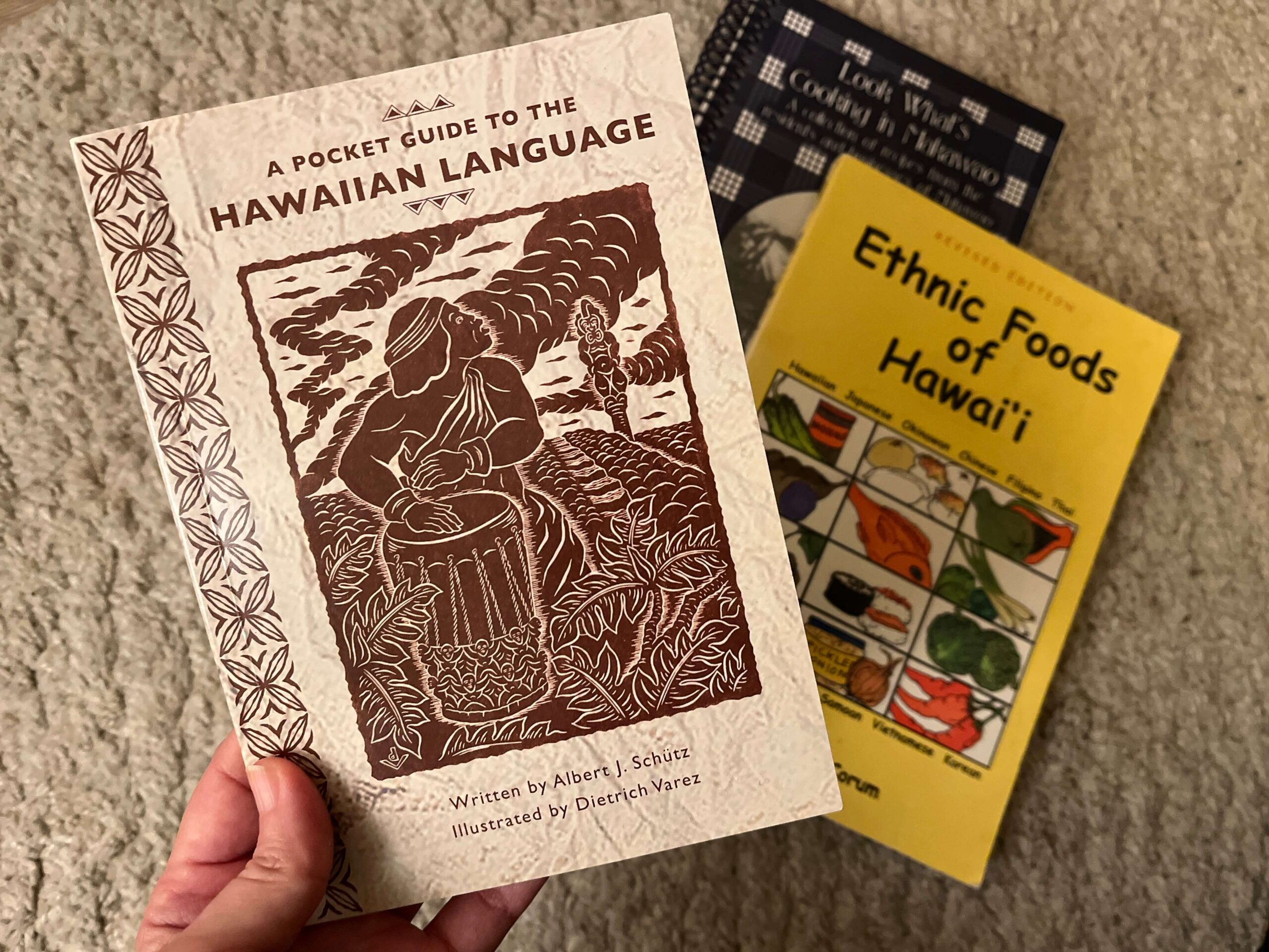 Learning about Olelo Hawaii - Hawaiian Language through online resources apps, and books like these 3 in the photo. In the foreground is A Pocket Guide to the Hawaiian language" and in the background, Ethnic Foods of Hawaii and another blue book that's blurred a bit.