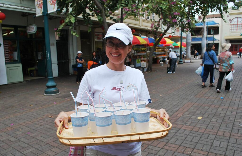 Malia Yoshioka leading a Hawaii food tour in Honolulu’s Chinatown, carrying a tray of drinks for guests.