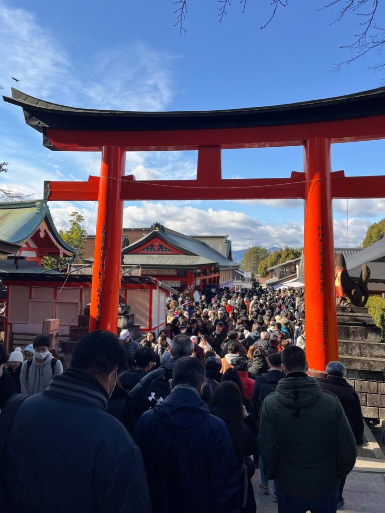 crowd at fushimi inari shrine in Kyoto around 11:30am on new years day 2026. the orange gate stands above a sea of people's heads attempting to leave the temple