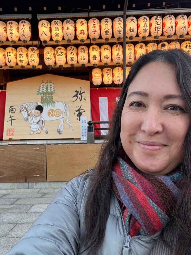 author Malia yoshioka visits yasaka shrine in gion, Kyoto on new years day in the year of the horse with lanterns lit and decorations celebrating the new year in the background

